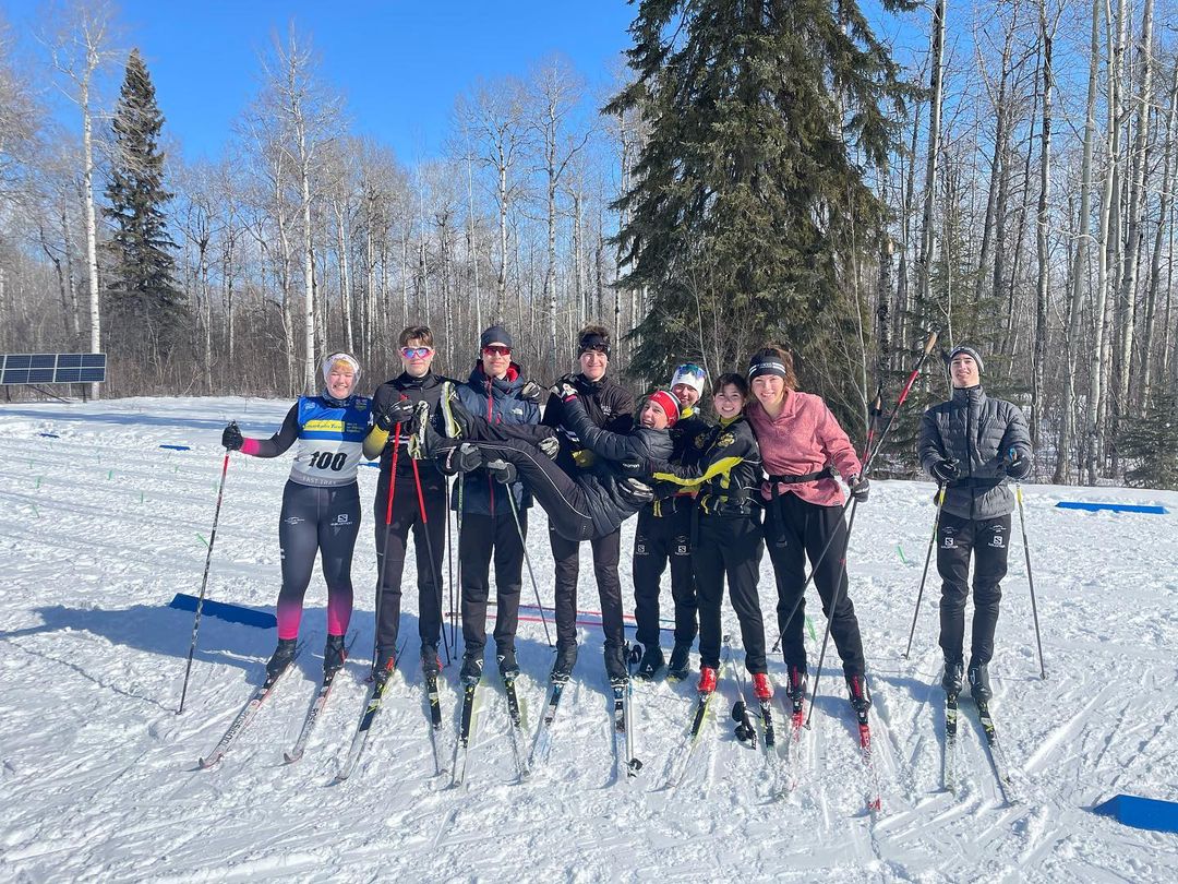 group of teens on nordic skis carrying another teen across them